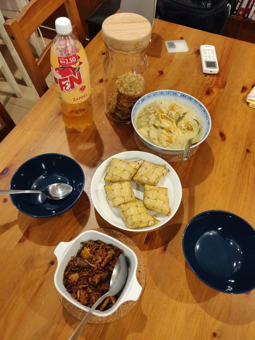 A table set for a small-scale hari raya feast. A casserole dish with sambal goreng, a plate of ketupat, a bowl of lodeh. 